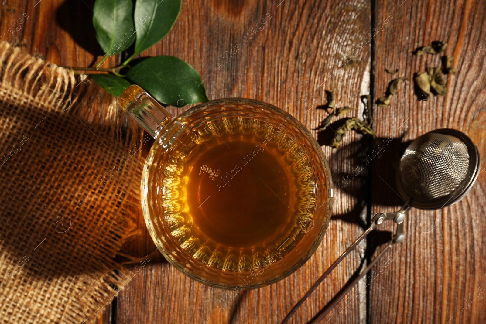 Photo of Refreshing green tea in cup, strainer and leaves on wooden table, flat lay