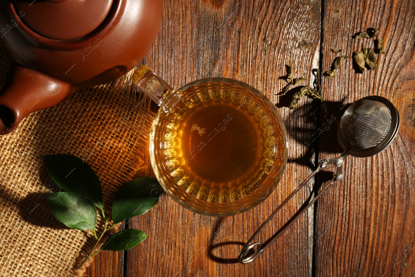 Photo of Refreshing green tea in cup, strainer and leaves on wooden table, flat lay