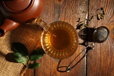 Photo of Refreshing green tea in cup, strainer and leaves on wooden table, flat lay