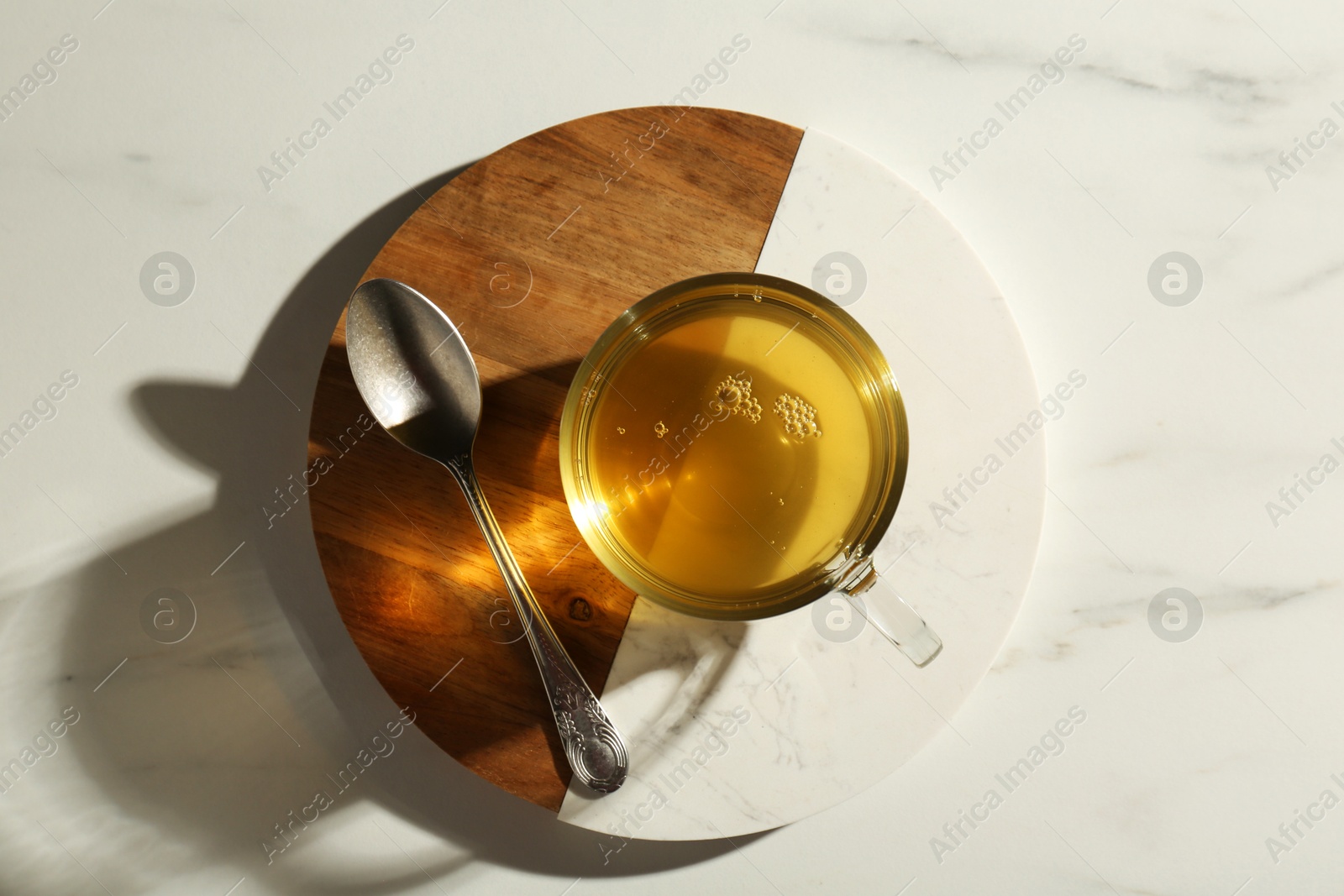 Photo of Refreshing green tea in cup and spoon on white marble table, top view