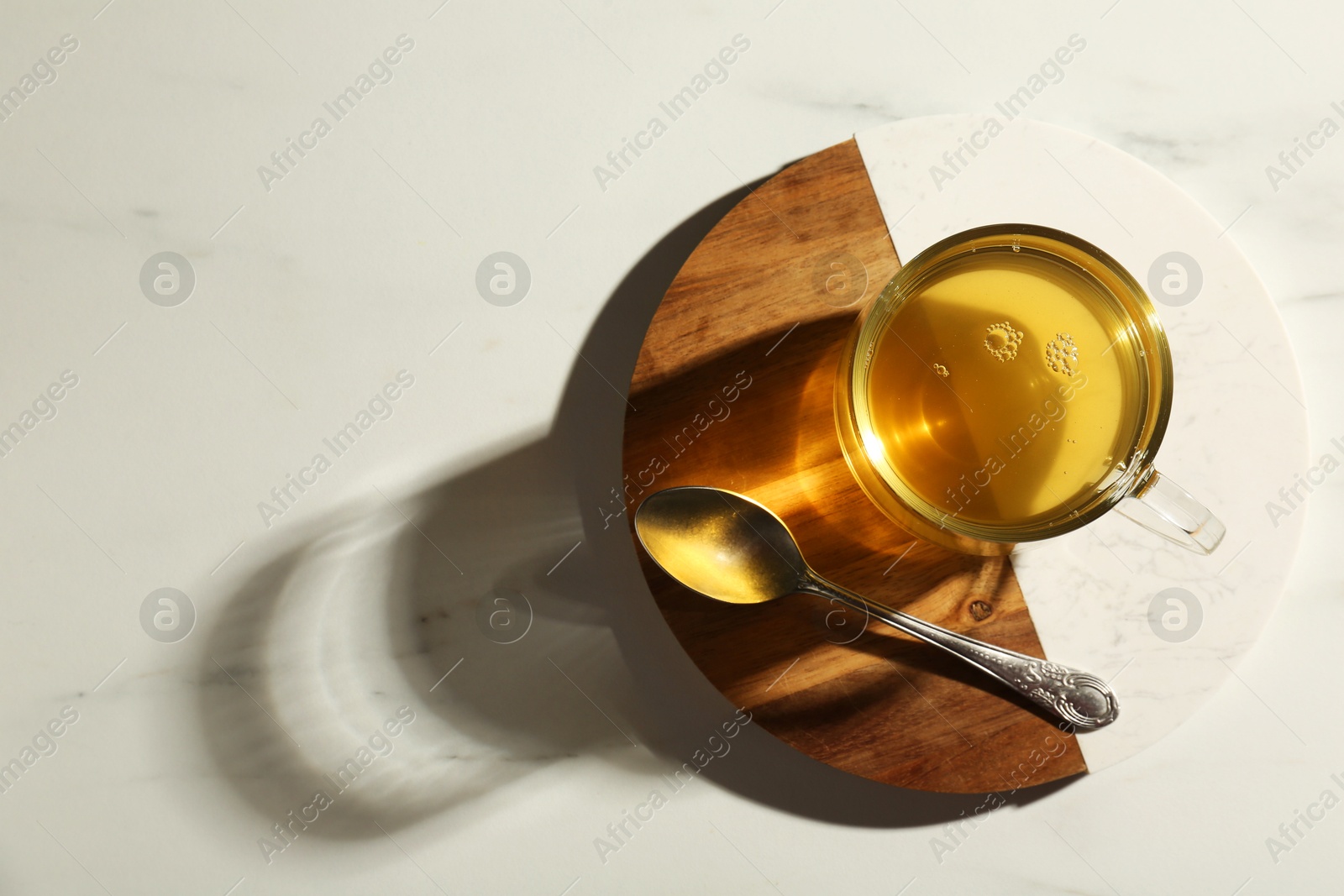 Photo of Refreshing green tea in cup and spoon on white marble table, top view. Space for text