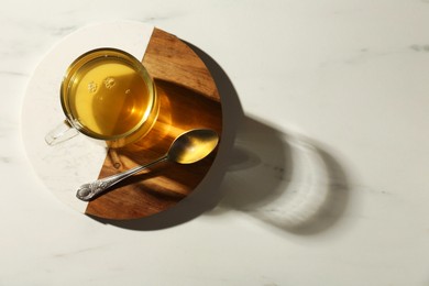 Photo of Refreshing green tea in cup and spoon on white marble table, top view. Space for text