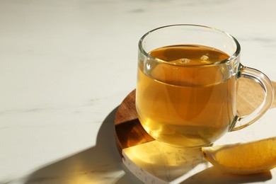 Photo of Refreshing green tea in cup and slice of lemon on white marble table, closeup. Space for text