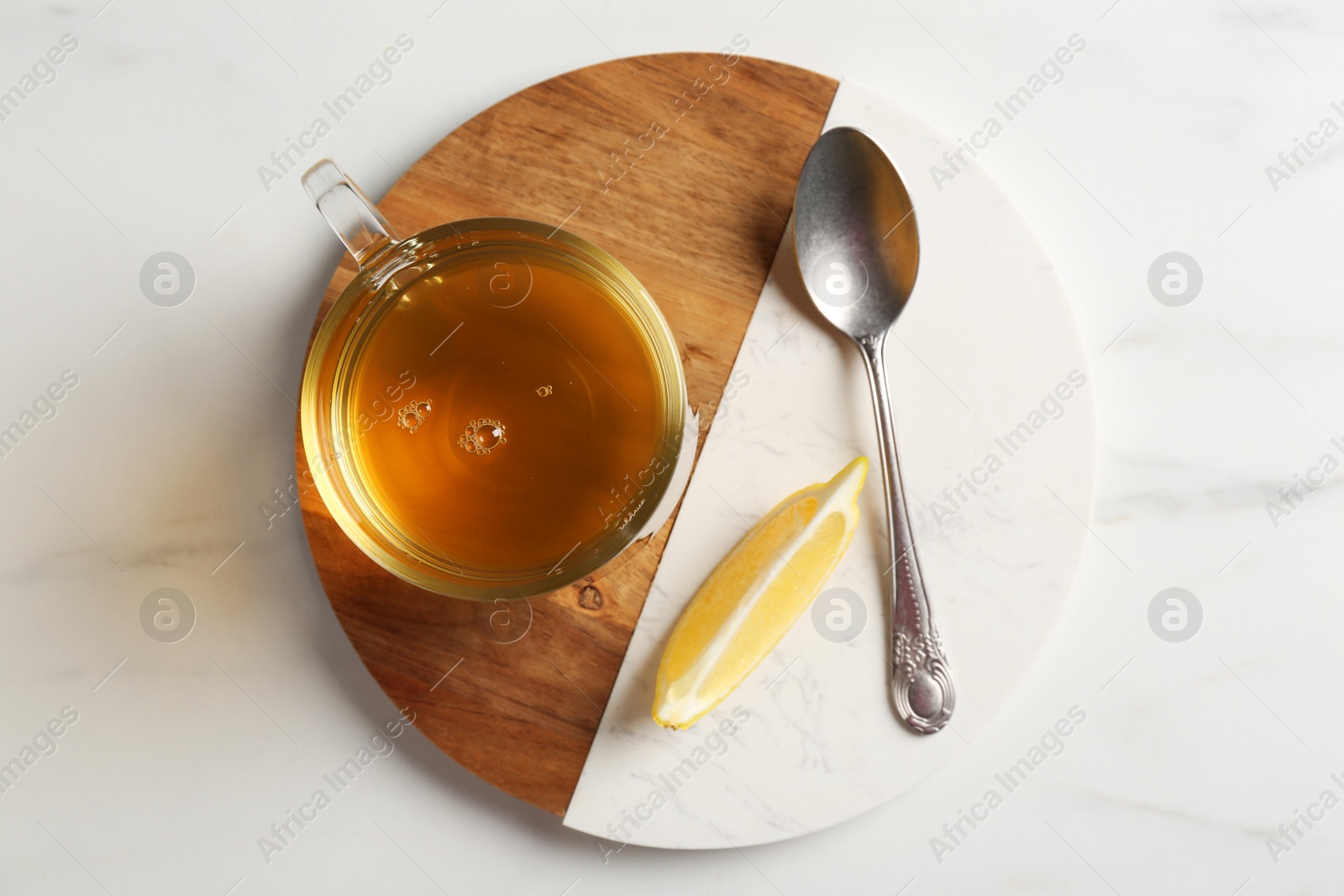 Photo of Refreshing green tea in cup, spoon and slice of lemon on white marble table, top view