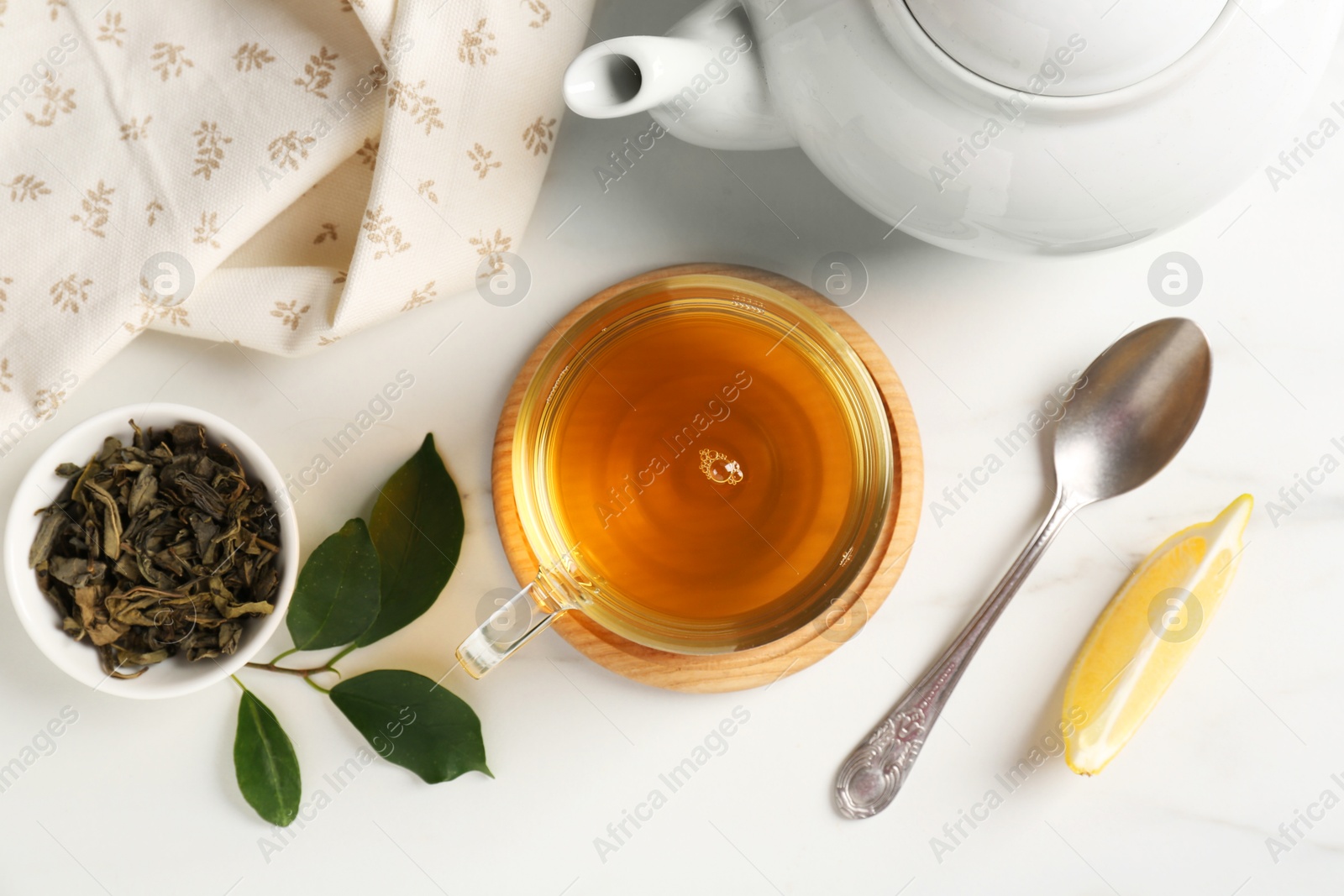 Photo of Refreshing green tea in cup, spoon, leaves and slice of lemon on white table, flat lay