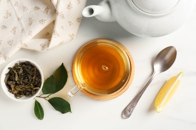 Photo of Refreshing green tea in cup, spoon, leaves and slice of lemon on white table, flat lay