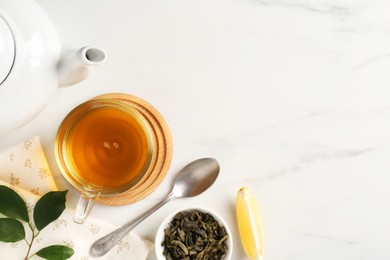 Photo of Refreshing green tea in cup, spoon, leaves and slice of lemon on white marble table, flat lay. Space for text