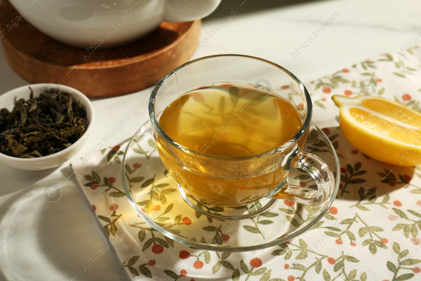 Photo of Refreshing green tea in cup, cut lemon and dry leaves on white table, closeup