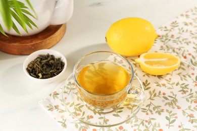 Refreshing green tea in cup, lemon and dry leaves on white table, closeup