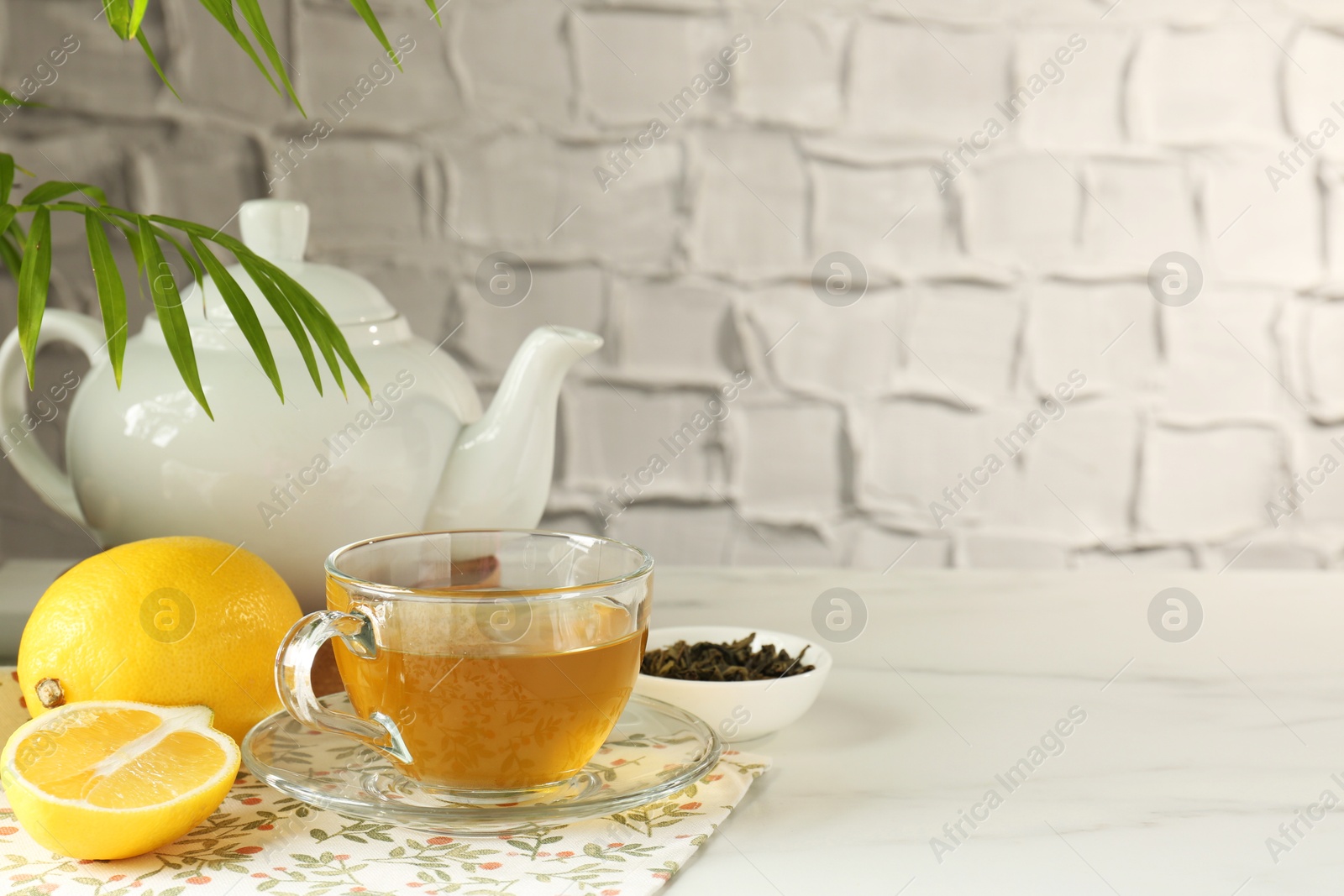 Photo of Refreshing green tea in cup, lemon and dry leaves on white marble table against textured wall. Space for text