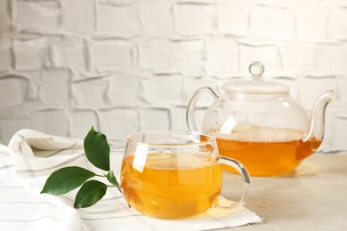 Photo of Refreshing green tea and leaves on light table against textured wall, closeup