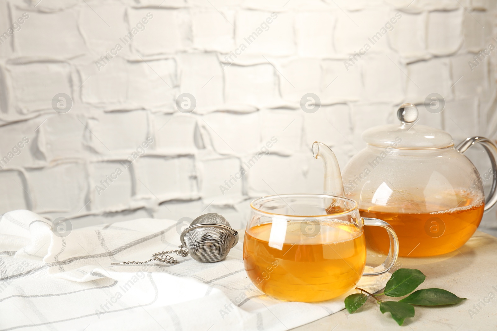 Photo of Refreshing green tea, strainer and leaves on light table against textured wall. Space for text