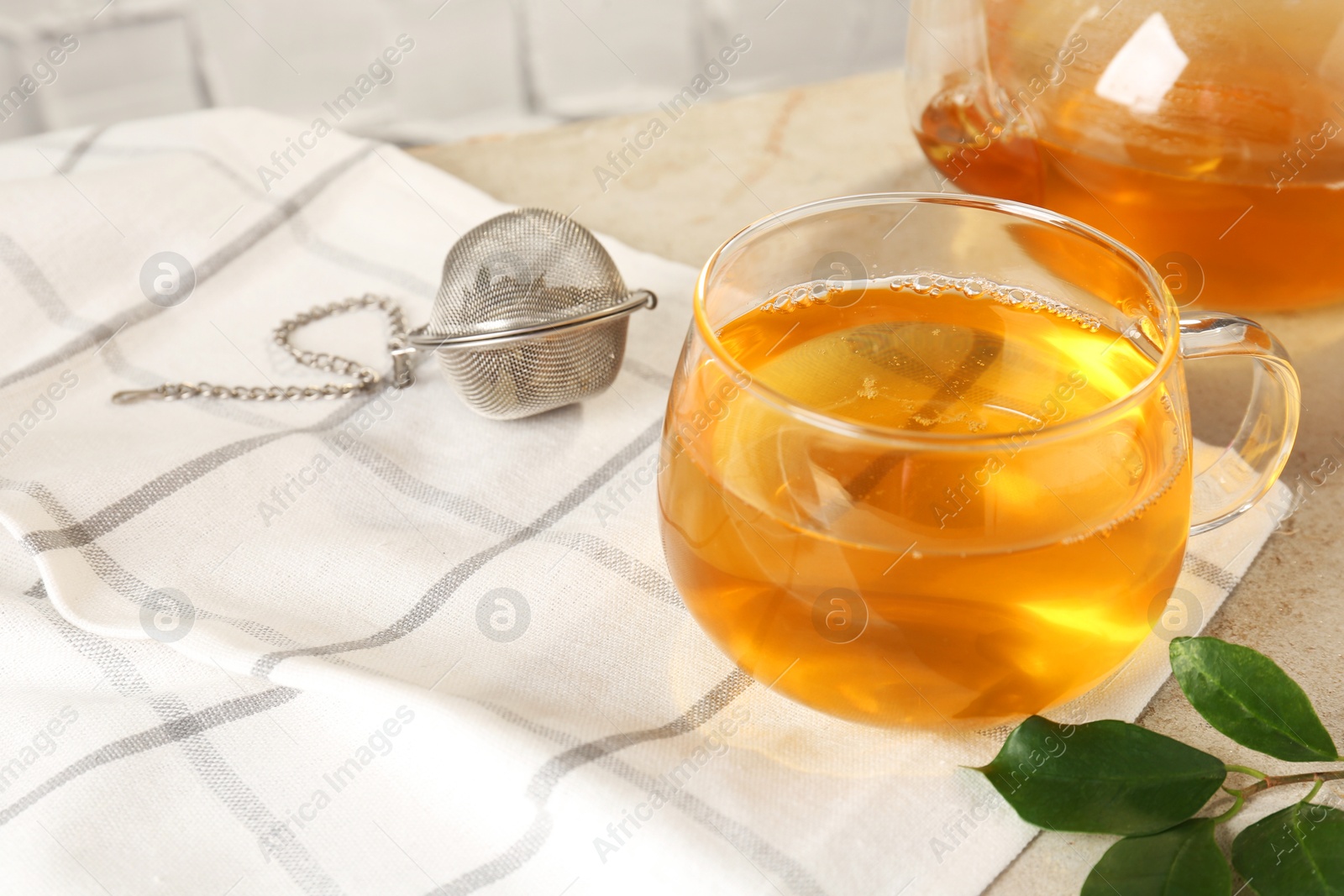 Photo of Refreshing green tea in cup, strainer and leaves on textured table, closeup