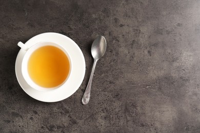 Photo of Refreshing green tea in cup and spoon on grey textured table, top view. Space for text