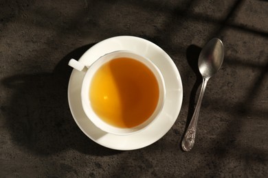 Refreshing green tea in cup and spoon on dark textured table, top view