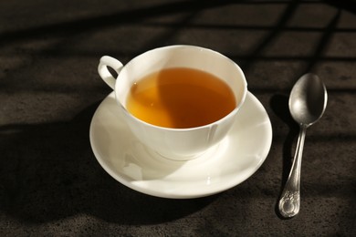 Photo of Refreshing green tea in cup and spoon on dark textured table, closeup