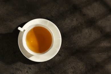 Photo of Refreshing green tea in cup on dark textured table, top view. Space for text