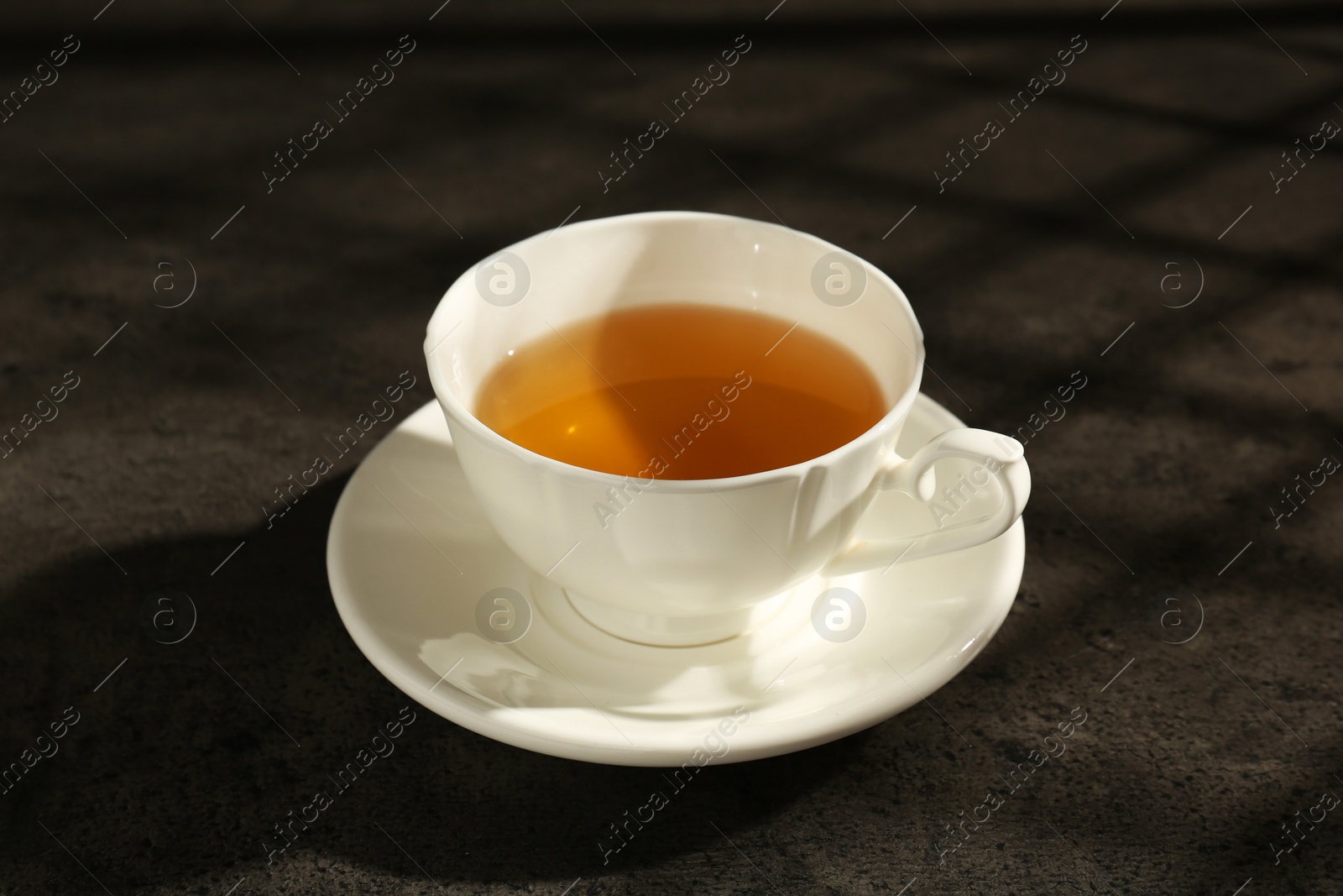 Photo of Refreshing green tea in cup on dark textured table, closeup