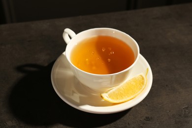 Photo of Refreshing green tea in cup and slice of lemon on dark textured table, closeup