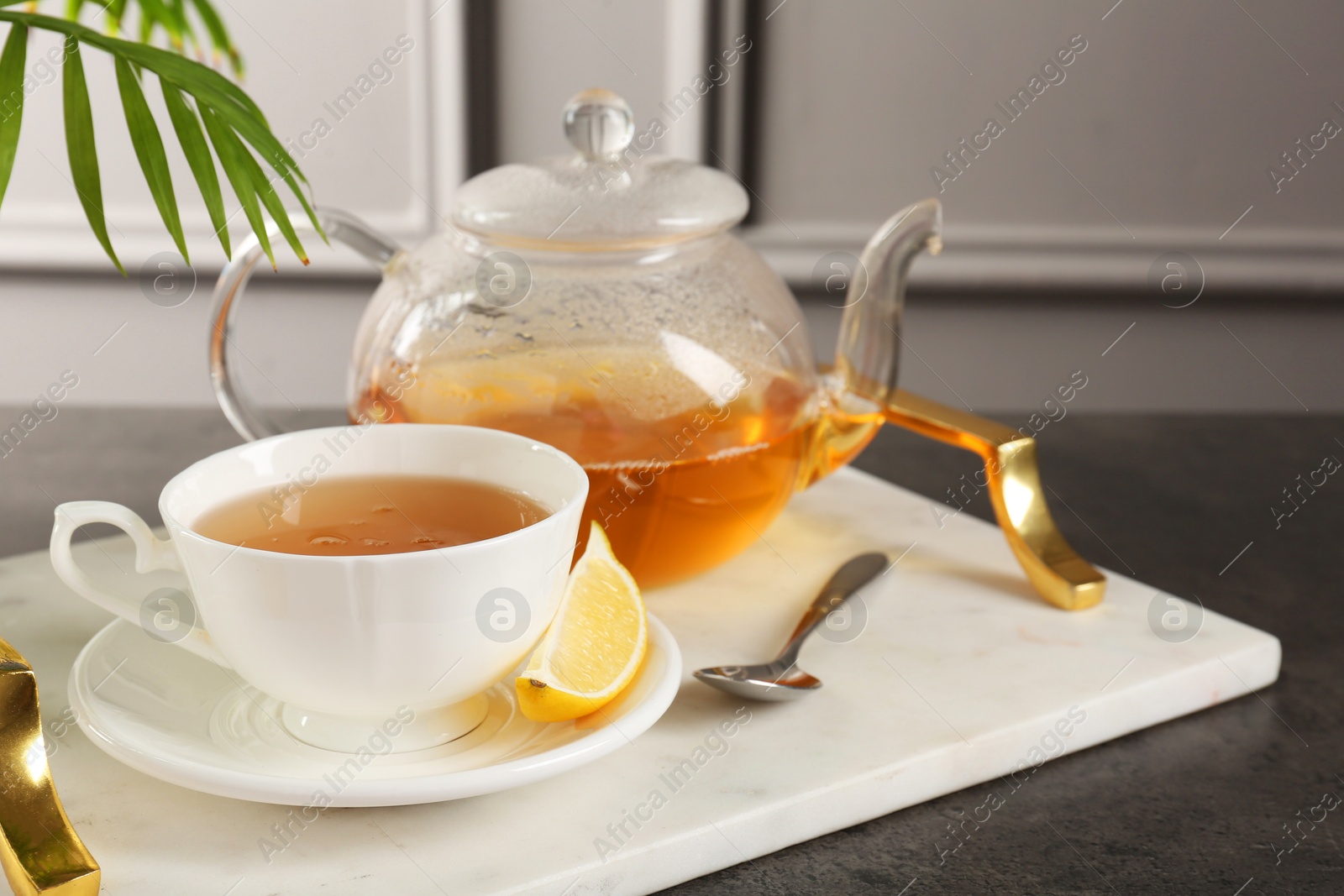 Photo of Refreshing green tea, spoon and slice of lemon on dark textured table