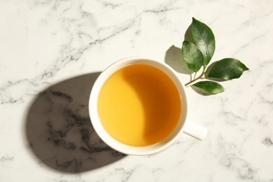 Refreshing green tea in cup and leaves on white marble table, top view