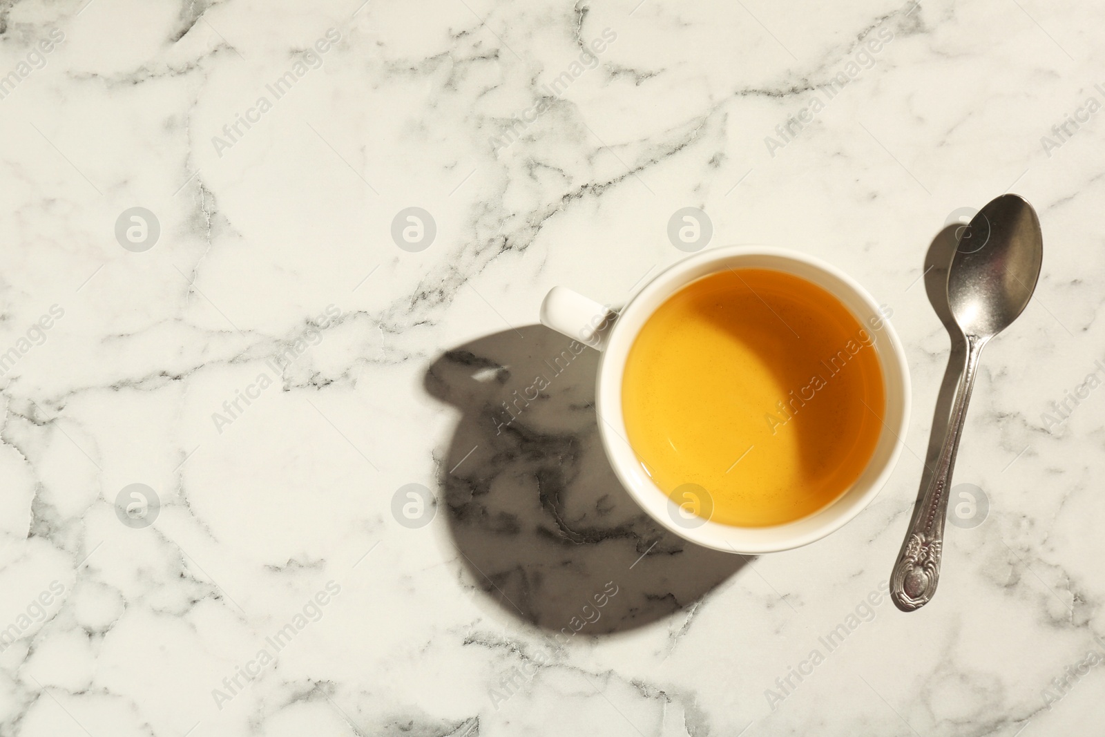 Photo of Refreshing green tea in cup and spoon on white marble table, top view. Space for text