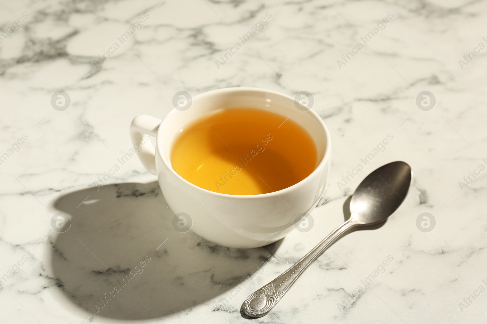 Photo of Refreshing green tea in cup and spoon on white marble table, closeup