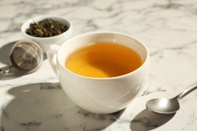 Photo of Refreshing green tea in cup and spoon on white marble table, closeup