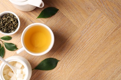 Photo of Refreshing green tea in cup, teapot, sugar bowl and leaves on wooden table, flat lay. Space for text