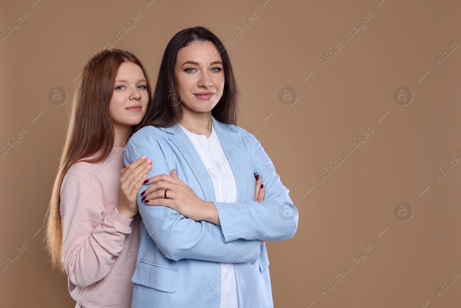 Photo of Portrait of beautiful mother with teenage daughter on dark beige background, space for text