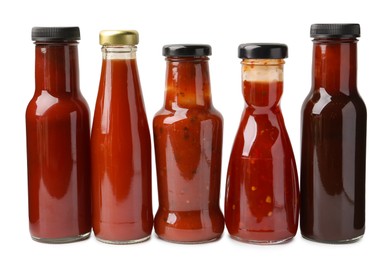 Photo of Different delicious sauces in glass bottles isolated on white