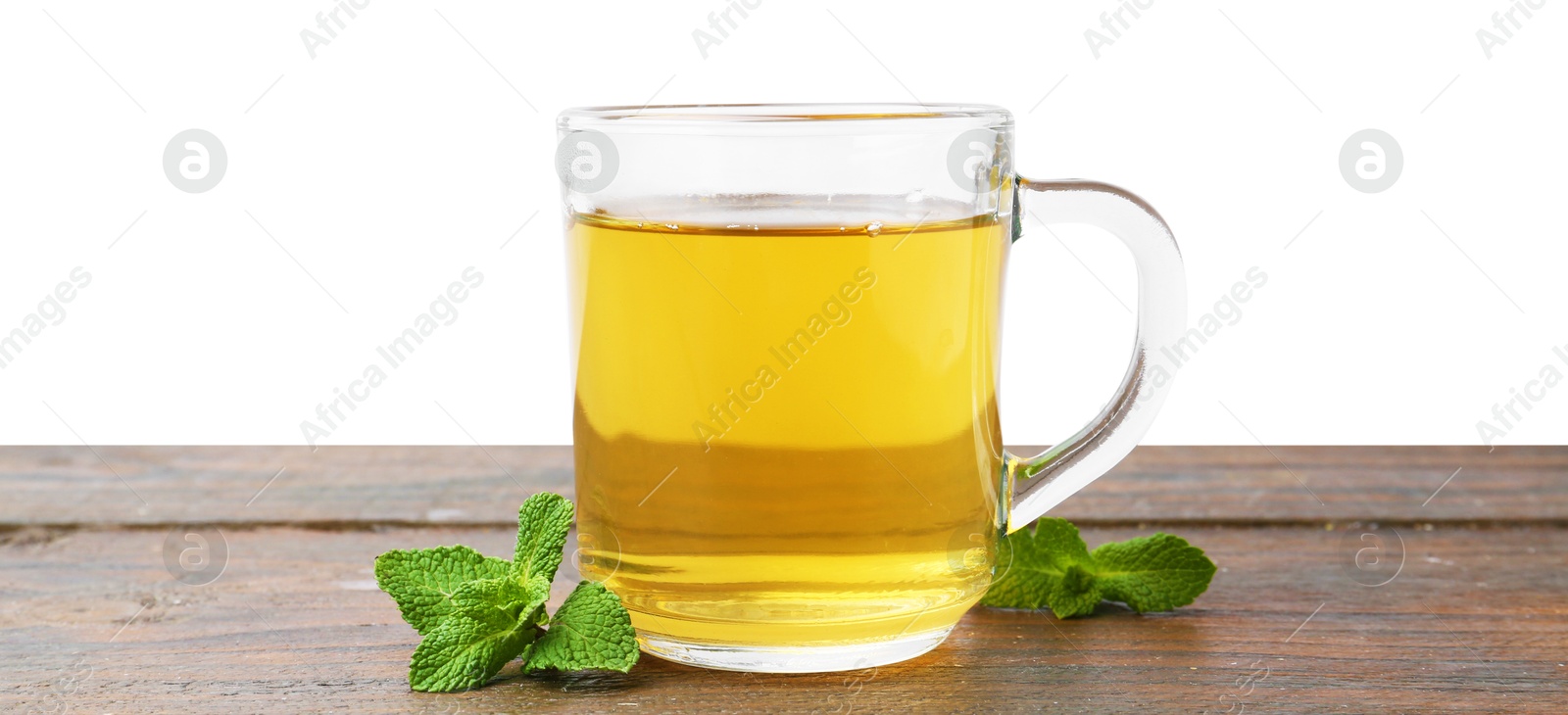 Photo of Aromatic mint tea in glass cup and fresh leaves on wooden table against white background