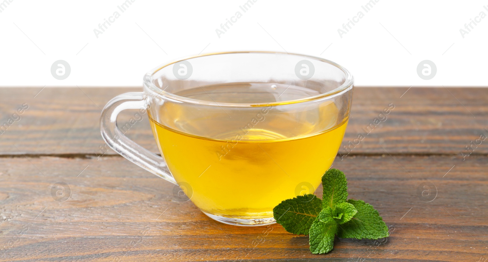 Photo of Aromatic mint tea in glass cup and fresh leaves on wooden table against white background