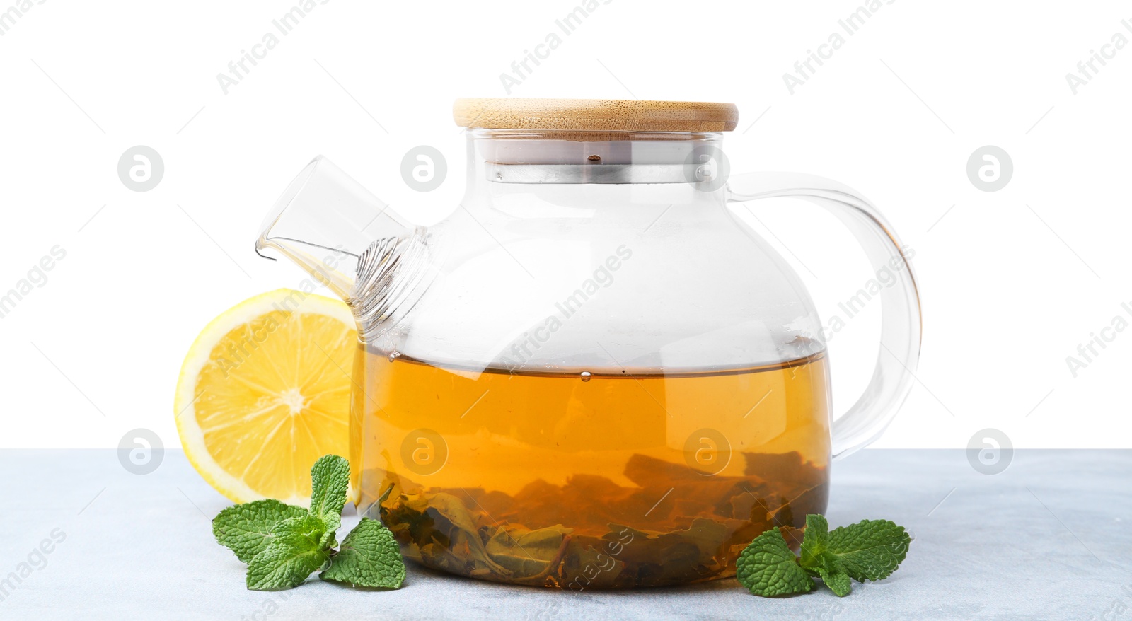 Photo of Aromatic mint tea in glass teapot, fresh leaves and lemon on light gray table against white background