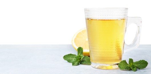 Photo of Aromatic mint tea in glass cup, fresh leaves and lemon on light gray table against white background, space for text