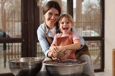 Photo of Hobby and craft. Smiling mother with her daughter making pottery indoors