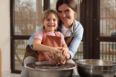 Photo of Hobby and craft. Smiling mother with her daughter making pottery indoors