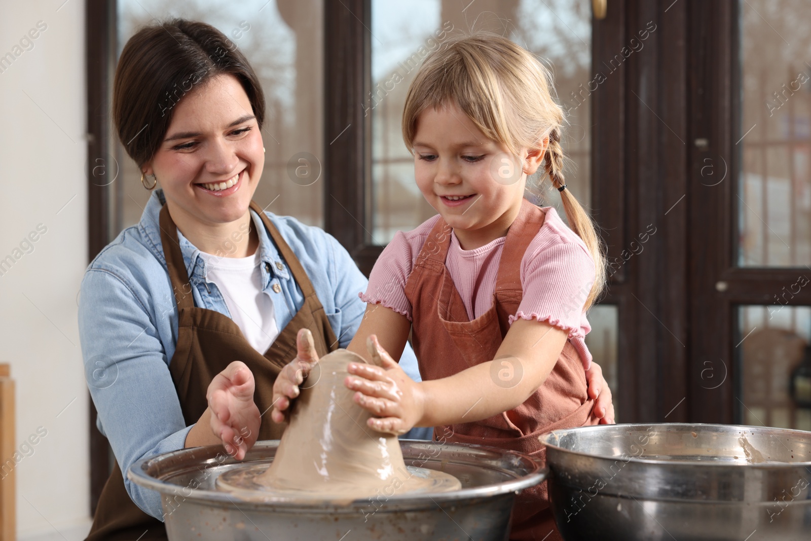 Photo of Hobby and craft. Smiling mother with her daughter making pottery indoors