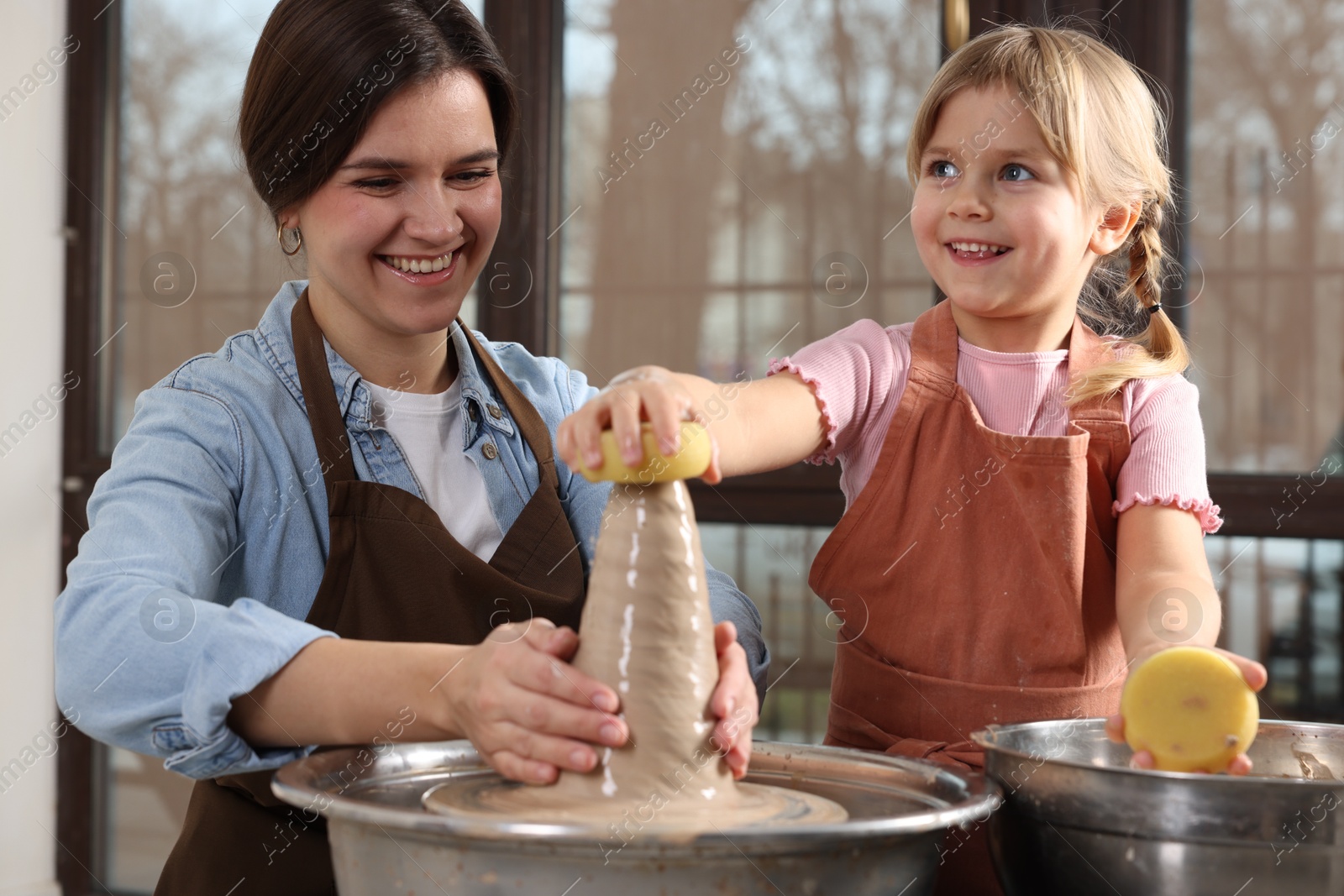 Photo of Hobby and craft. Smiling mother with her daughter making pottery indoors