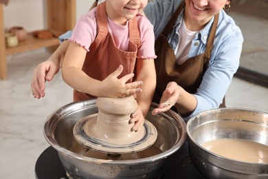 Photo of Hobby and craft. Smiling mother with her daughter making pottery indoors, closeup