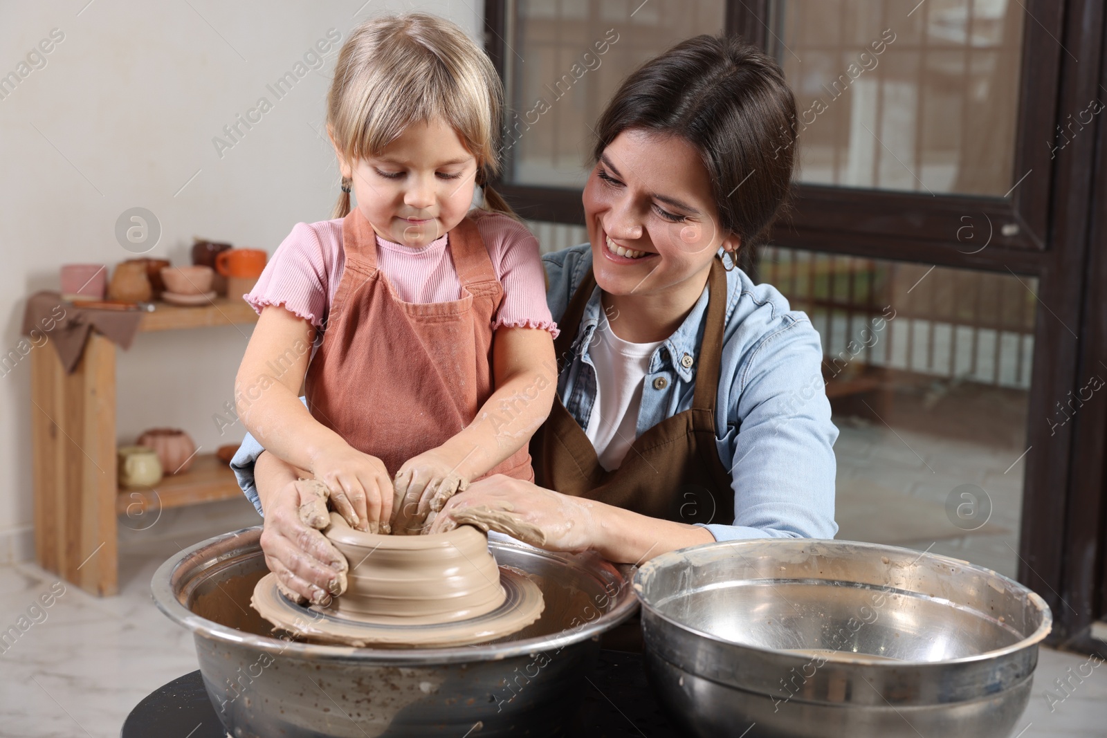 Photo of Hobby and craft. Smiling mother with her daughter making pottery indoors