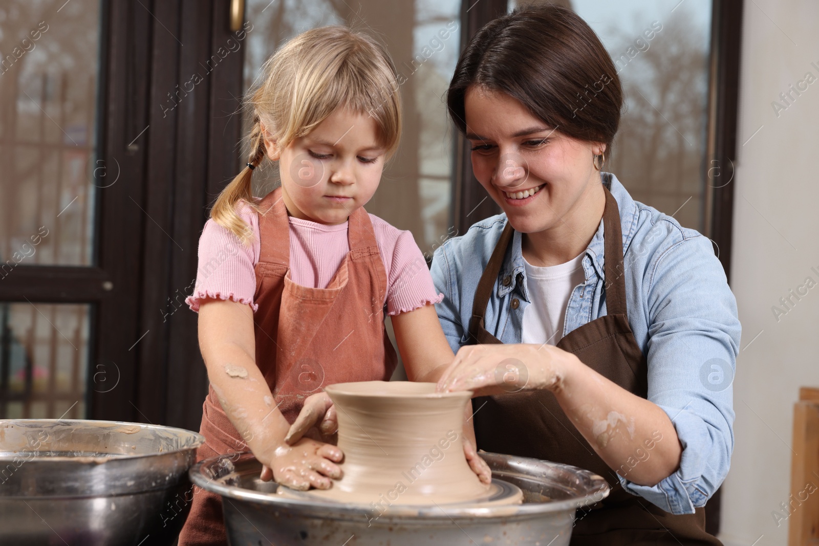 Photo of Hobby and craft. Smiling mother with her daughter making pottery indoors