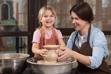 Photo of Hobby and craft. Smiling mother with her daughter making pottery indoors