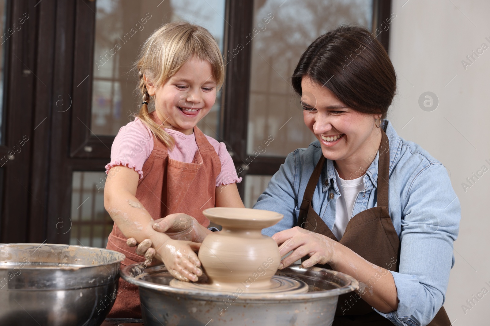 Photo of Hobby and craft. Smiling mother with her daughter making pottery indoors