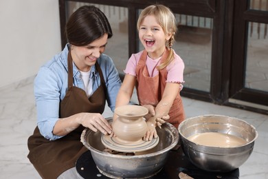 Photo of Hobby and craft. Smiling mother with her daughter making pottery indoors