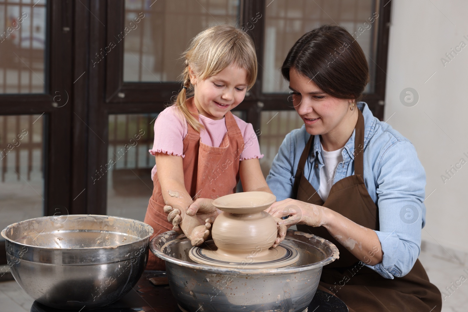 Photo of Hobby and craft. Smiling mother with her daughter making pottery indoors