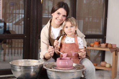 Photo of Hobby and craft. Smiling mother with her daughter making pottery indoors