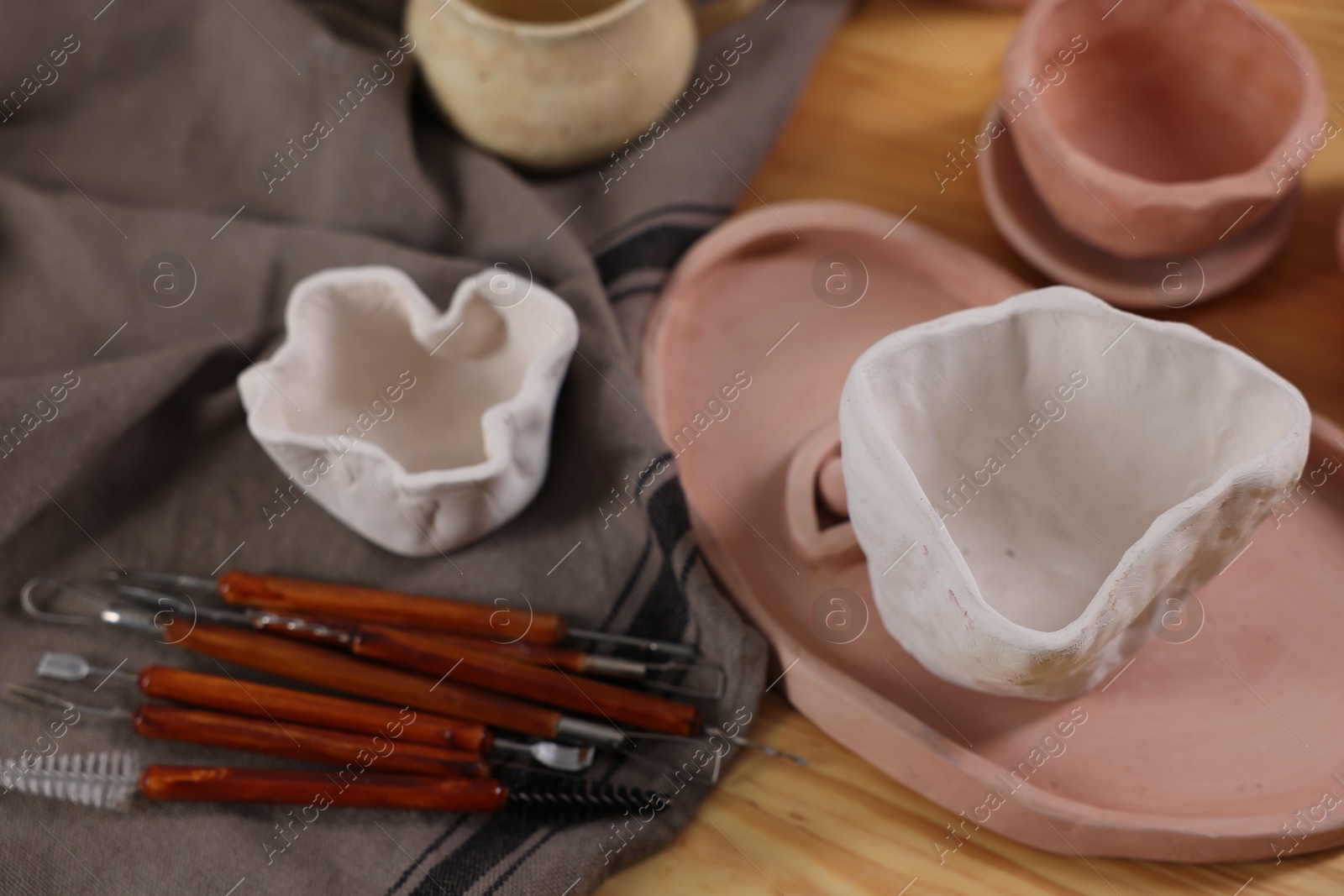 Photo of Set of different clay crafting tools and pottery on wooden table, above view