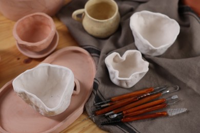 Photo of Set of different clay crafting tools and pottery on wooden table, above view