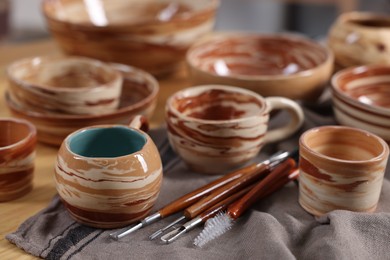 Photo of Different beautiful pottery and set of clay crafting tools on wooden table, closeup